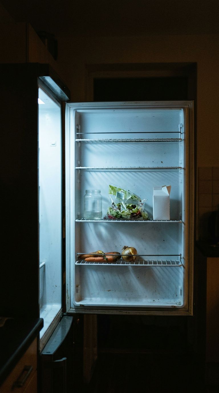 An open fridge at night with almost empty shelves